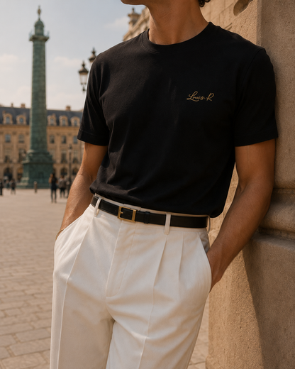 Un homme portant le T shirt noir Louis.R à la place Vendome de Paris, combinant un pantalon blanc afin de ressortir davantage la couleur dorée du logo et sa silouhette.